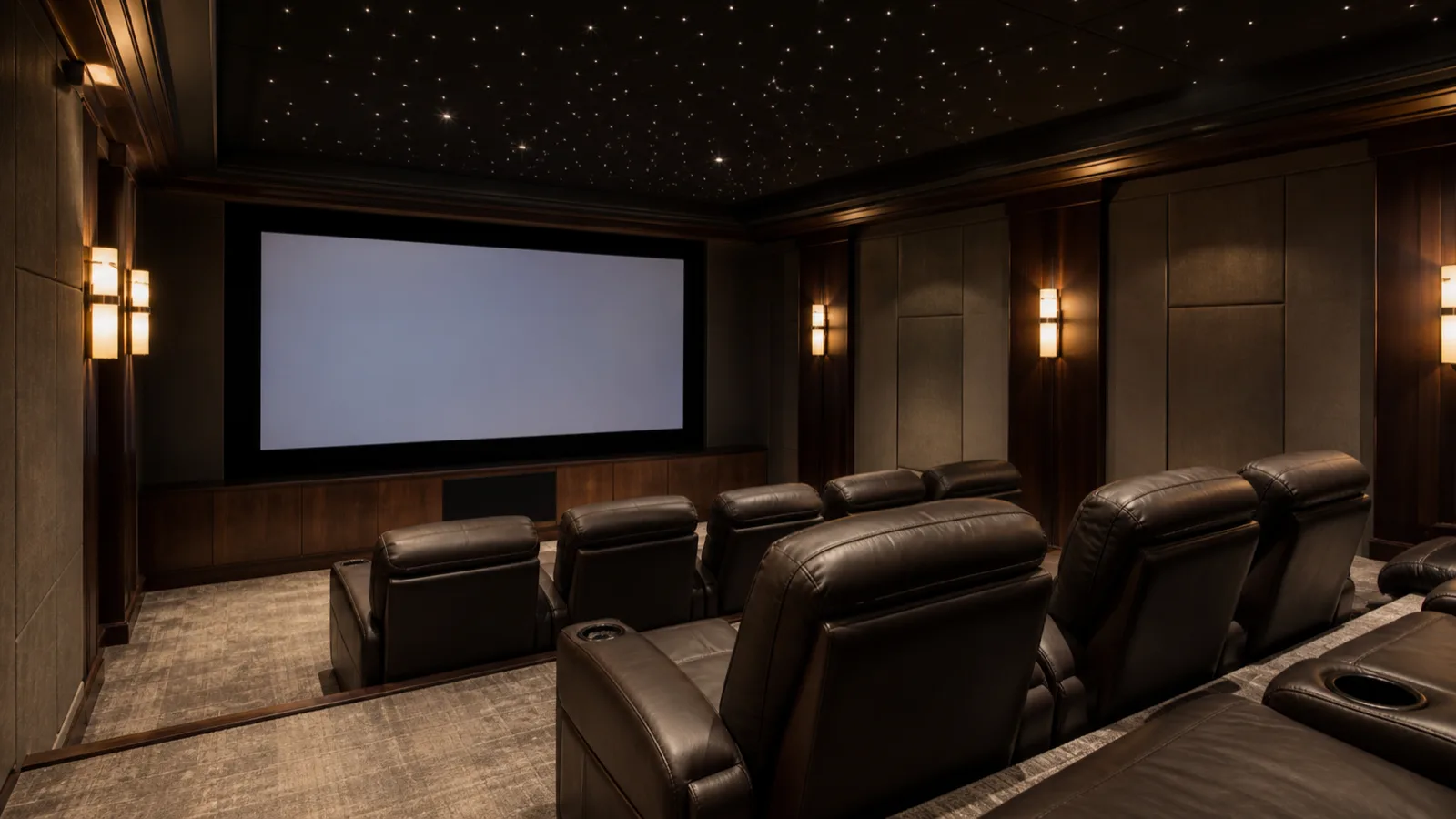 A luxury home theater with tiered recliner seating, wide screen, star-field ceiling and side sconces.