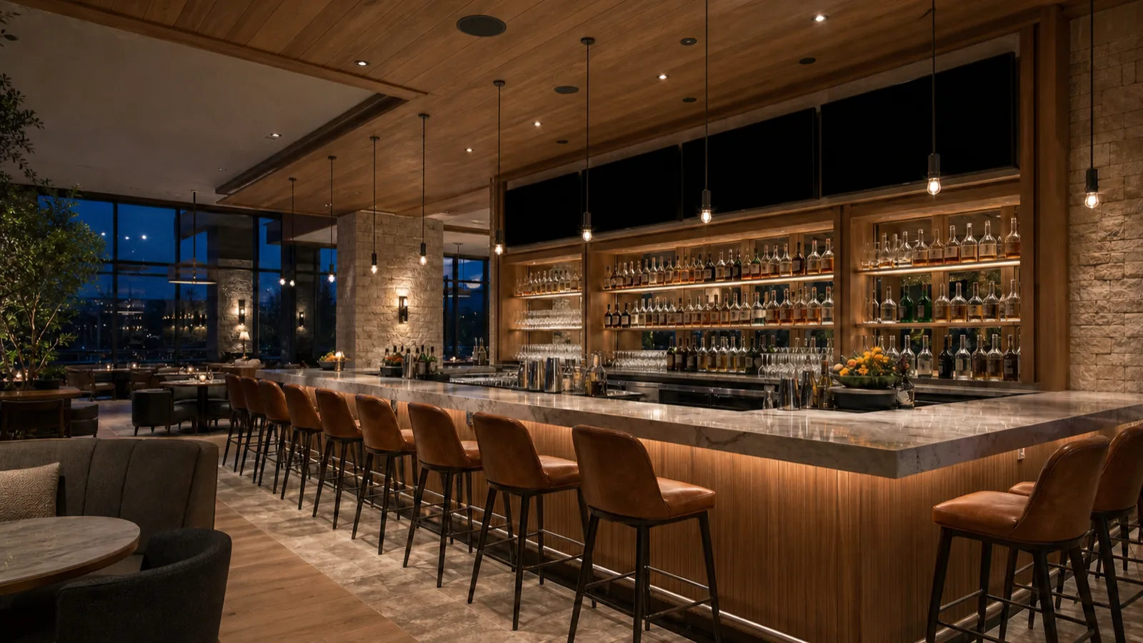 An upscale restaurant bar interior in the evening with discreet ceiling speakers and blank dark screens above the back bar.