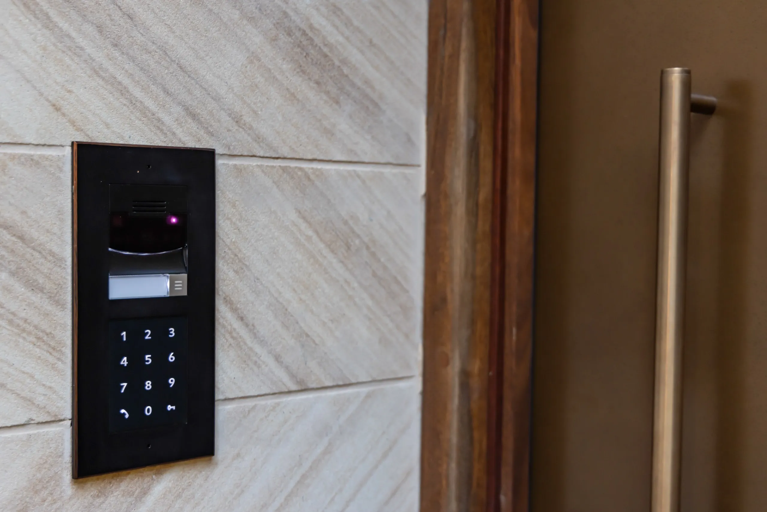 Black electronic door keypad and card reader mounted on light stone tile next to a metal door handle.
