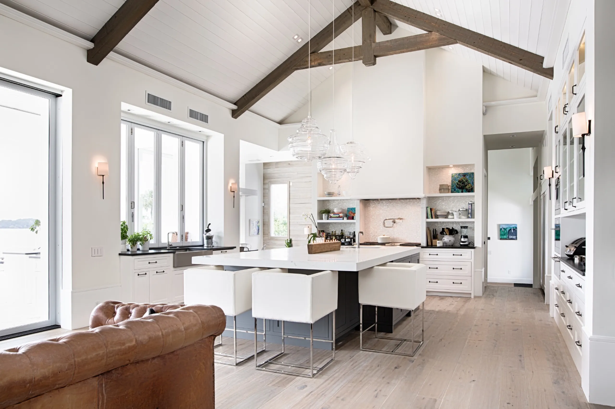 Bright luxury kitchen with a white island, glass pendants, and vaulted ceiling with dark wood beams.