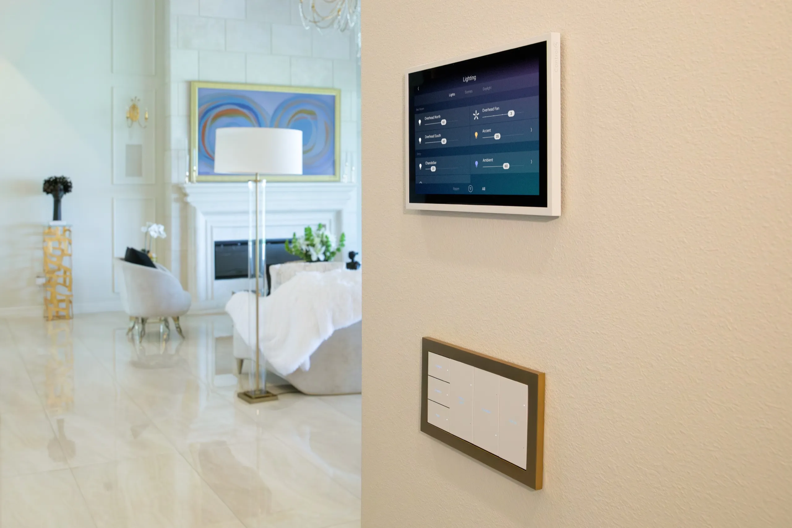 Wall-mounted smart touchscreen showing lighting controls above a multi-button keypad, opening to a bright bedroom suite.