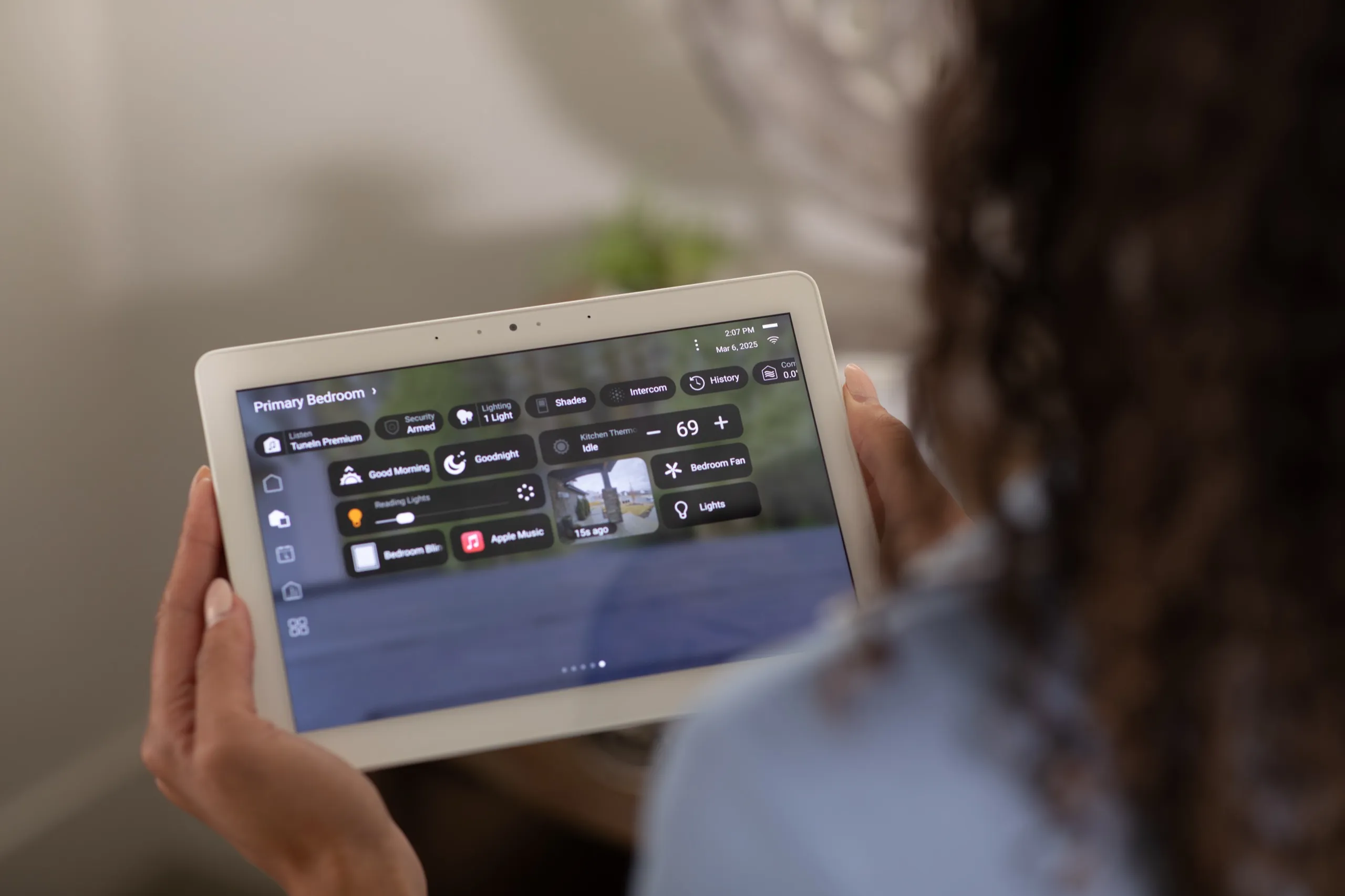 Hands holding a white tablet showing a primary bedroom control screen with security armed status.