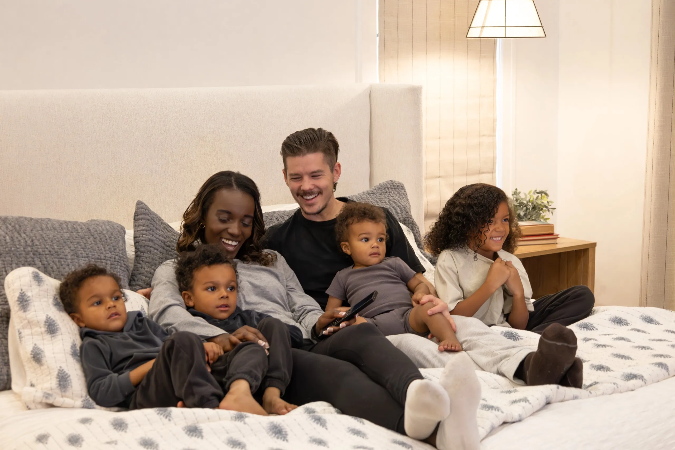 Family of six sitting on a bed together smiling while watching entertainment.