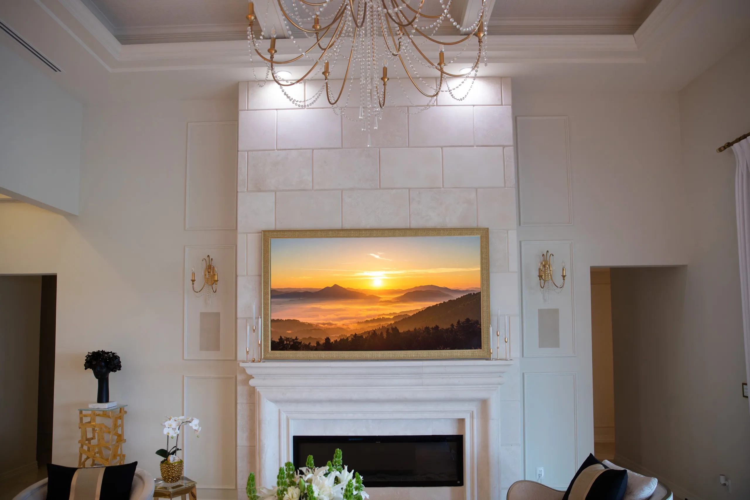 Luxury living room with a large framed television above a marble fireplace under a crystal chandelier.