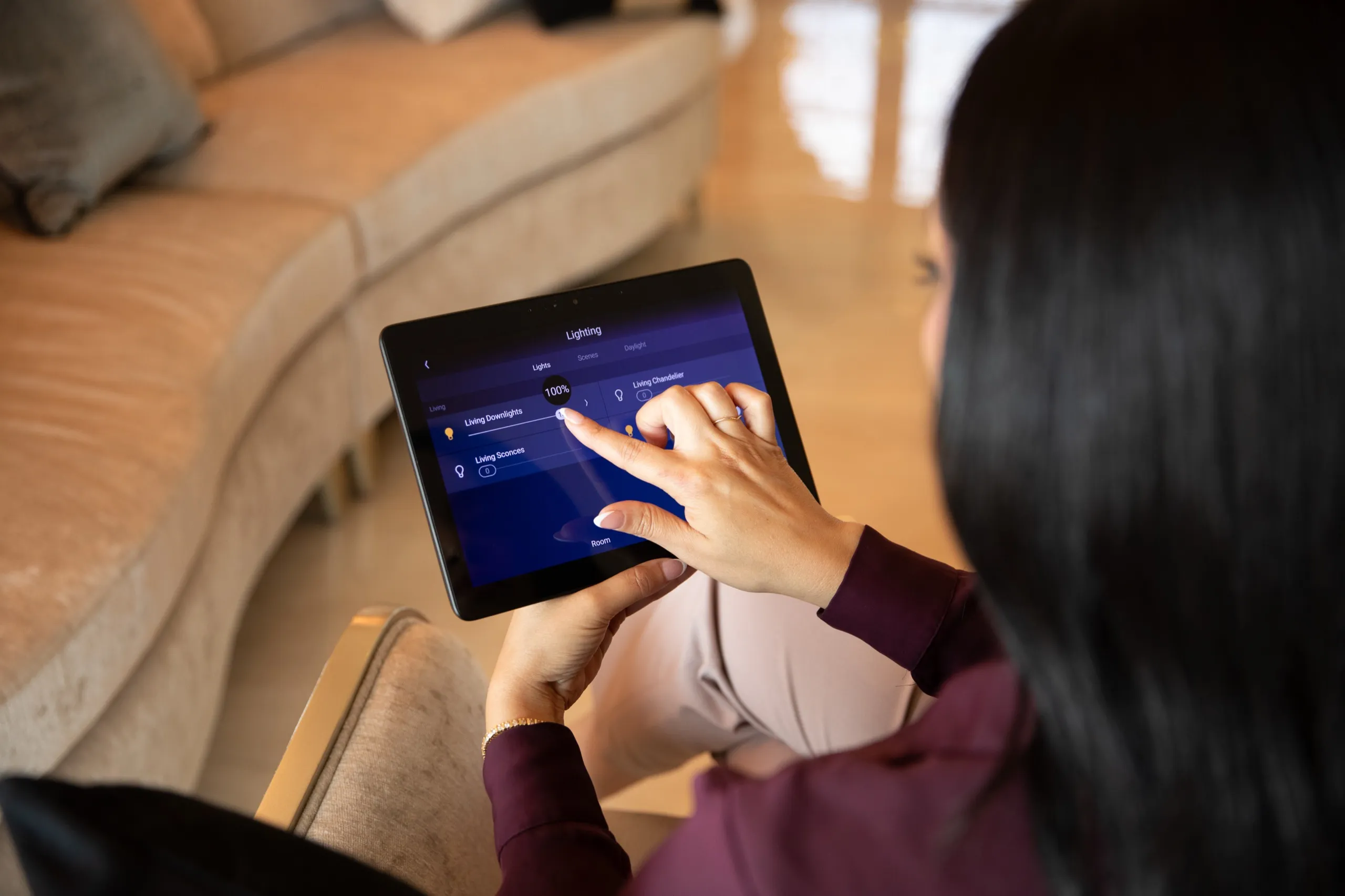 Woman adjusting living-room lighting levels on a tablet control app.