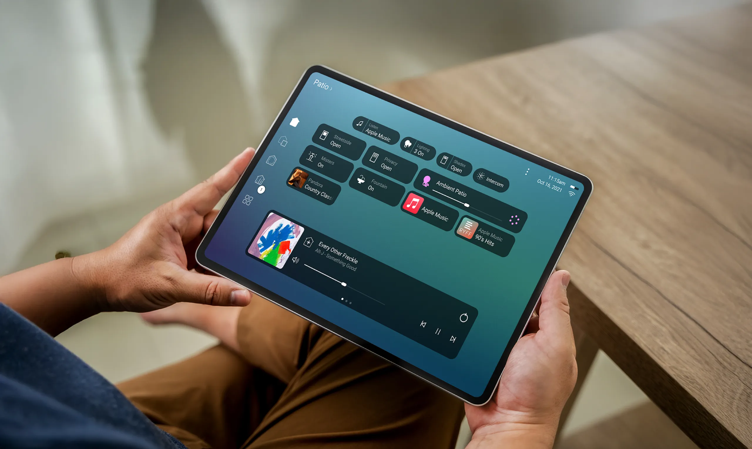 Hands holding a tablet showing a control screen for patio lighting, shades, and music.