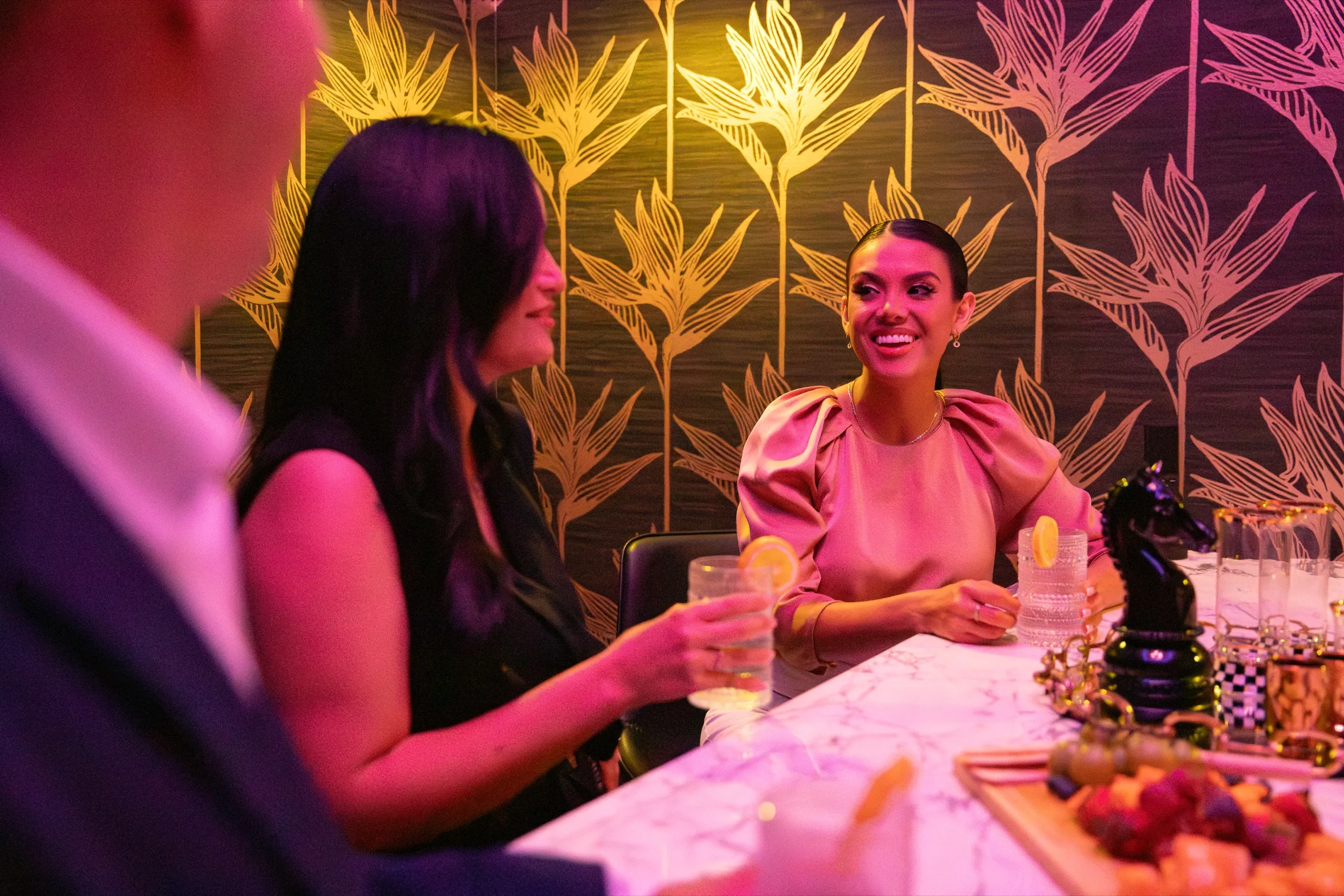 Guests at a white marble bar with even, layered lighting and background music speakers overhead.