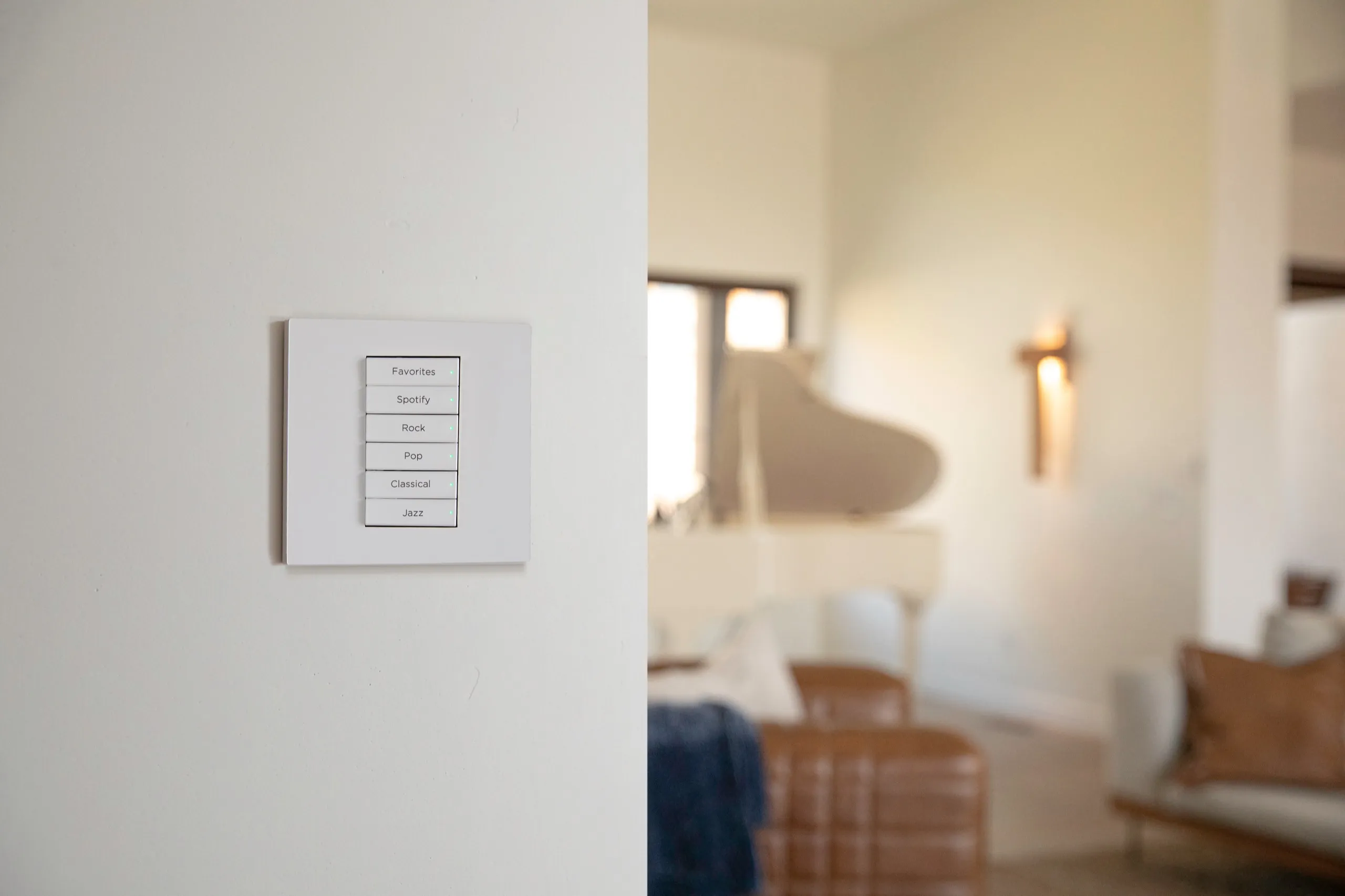 White wall keypad with music genre buttons beside a softly blurred living room with a piano.