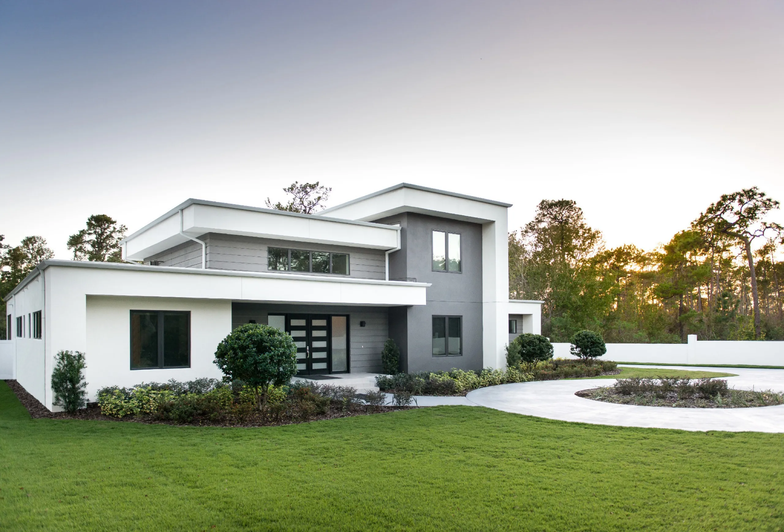 Modern two-story white and gray commercial-style building with a flat roof and circular driveway under pale sky.