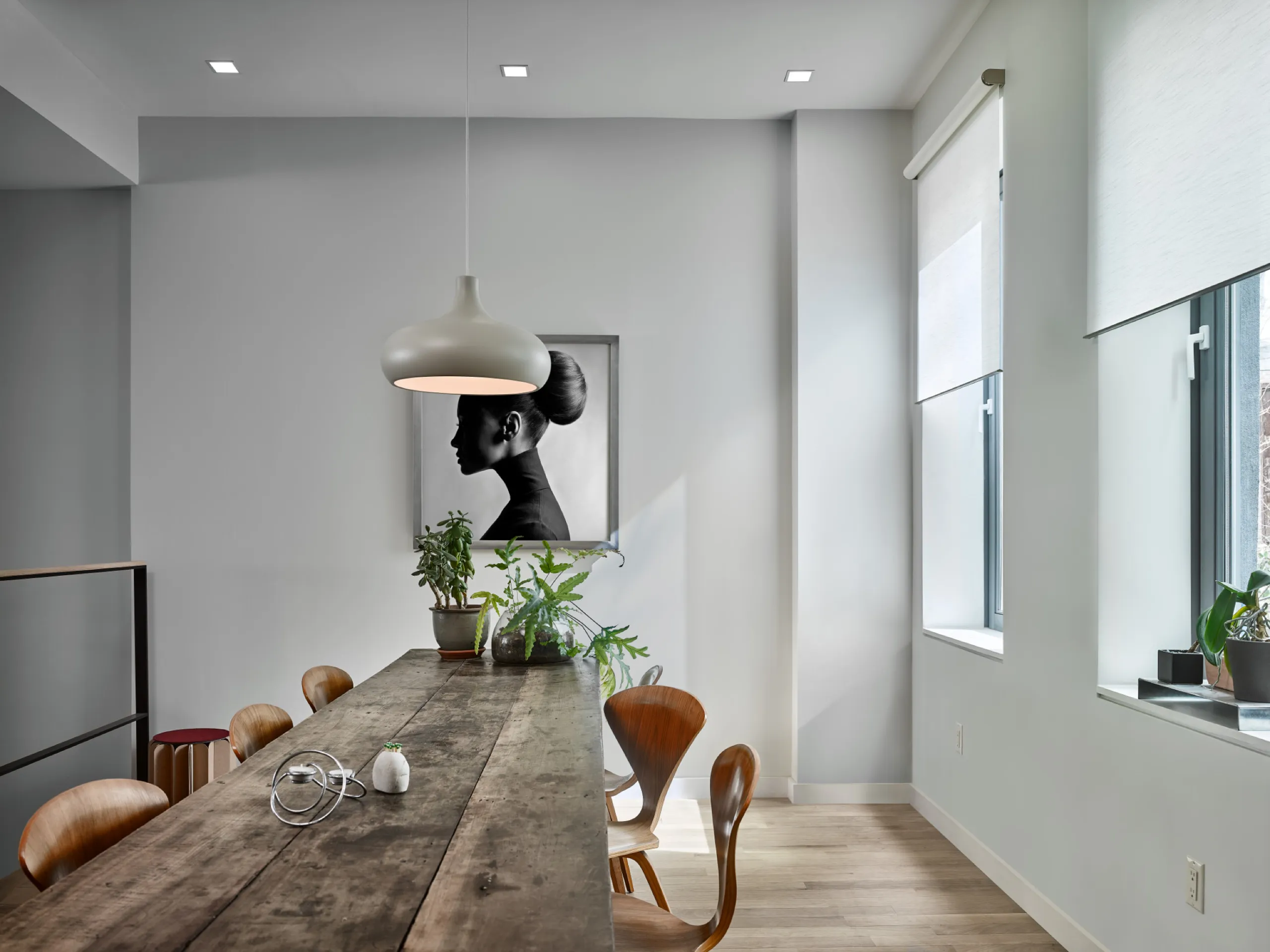 Loft dining room with long wood table, teardrop pendant, white roller shades, and a large profile portrait