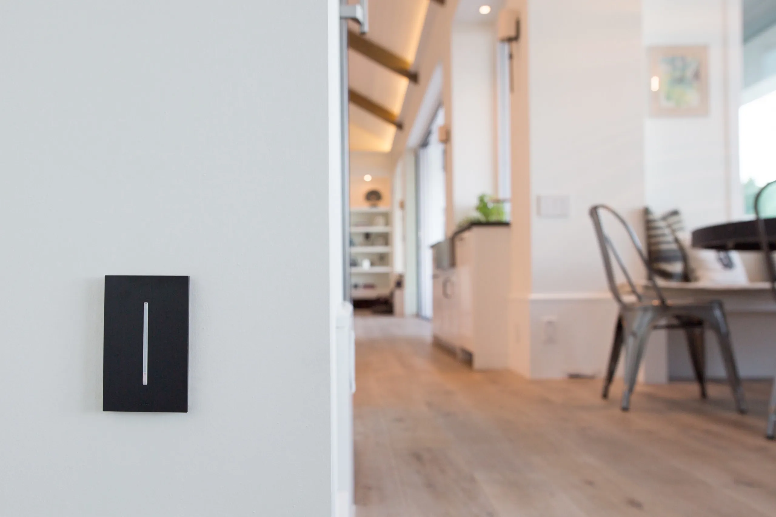 Black Lutron Grafik T dimmer with a vertical light bar on a white wall, soft-focus luxury kitchen beyond.