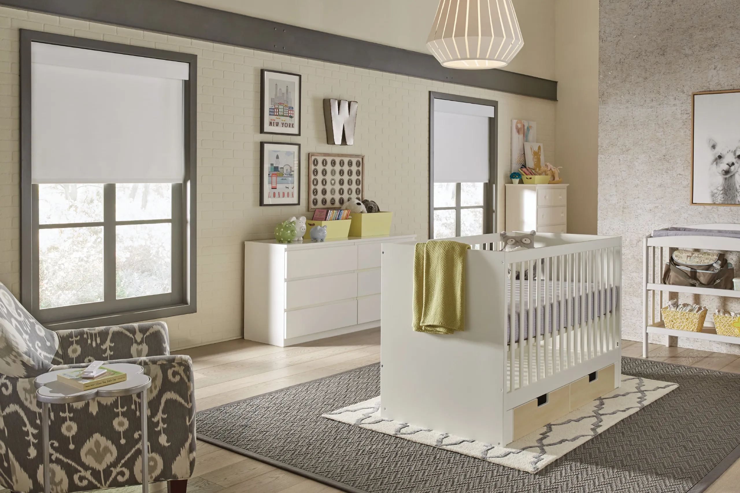 Modern nursery with white furniture, partially drawn roller shades, and a Lutron Pico remote on a side table.