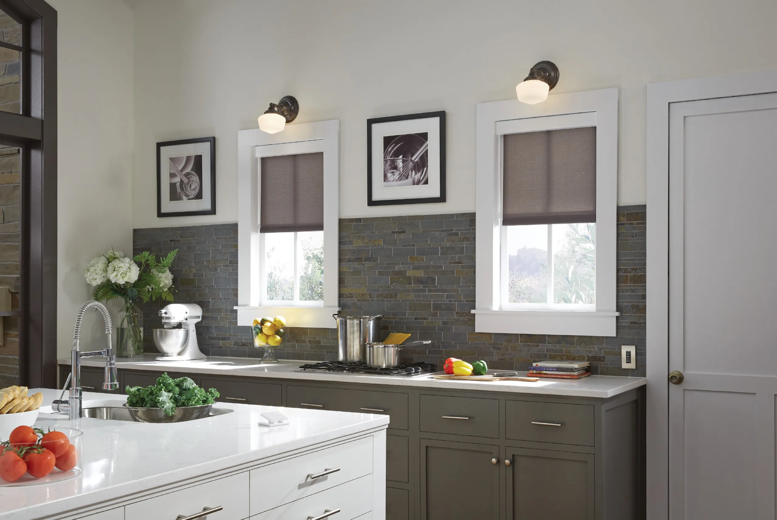 Modern kitchen with olive cabinets, dark stone backsplash, and matching charcoal roller shades on two windows.