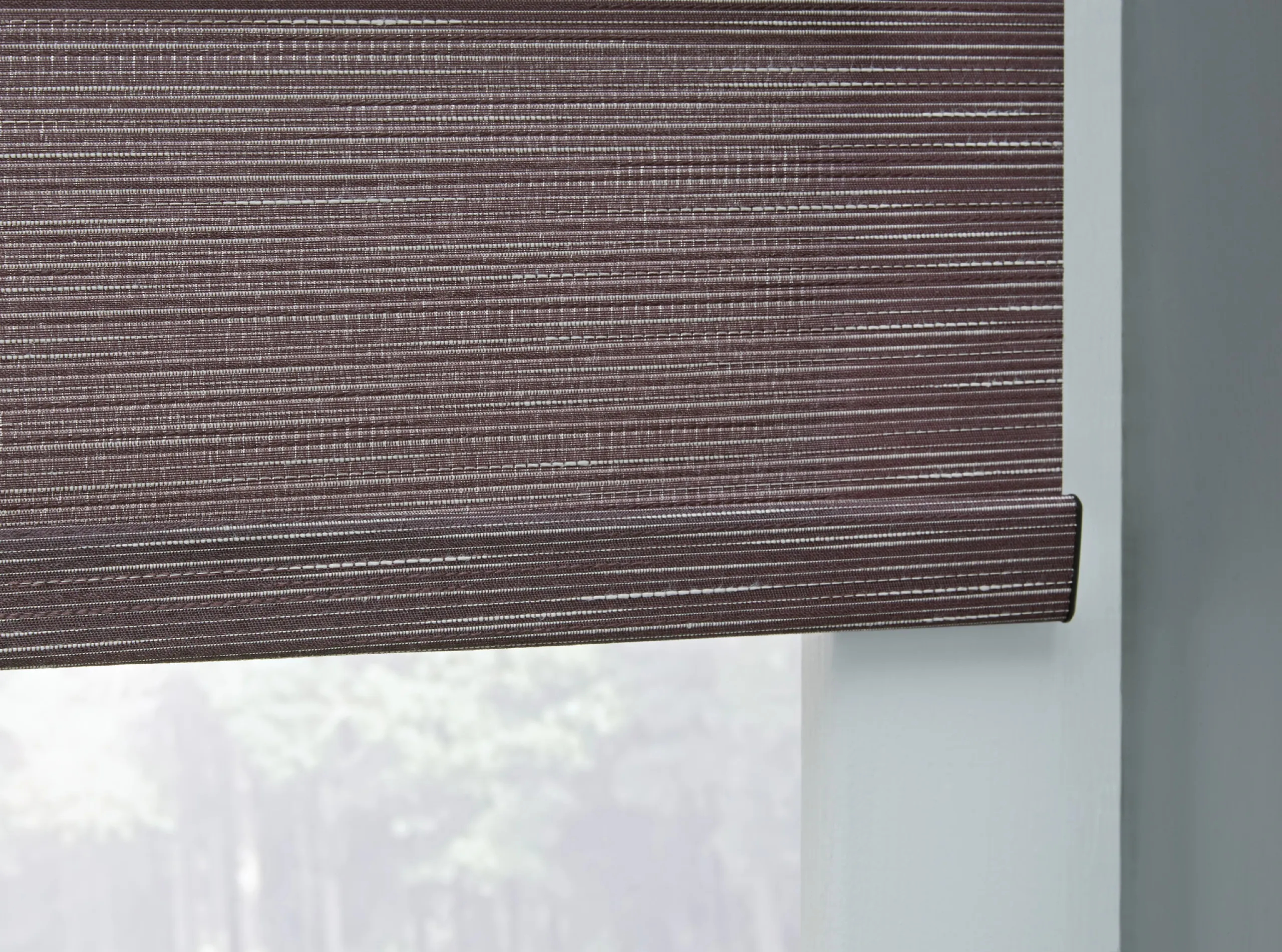 Detail of a dark charcoal textured Lutron roller shade and matching hembar above a bright window view.