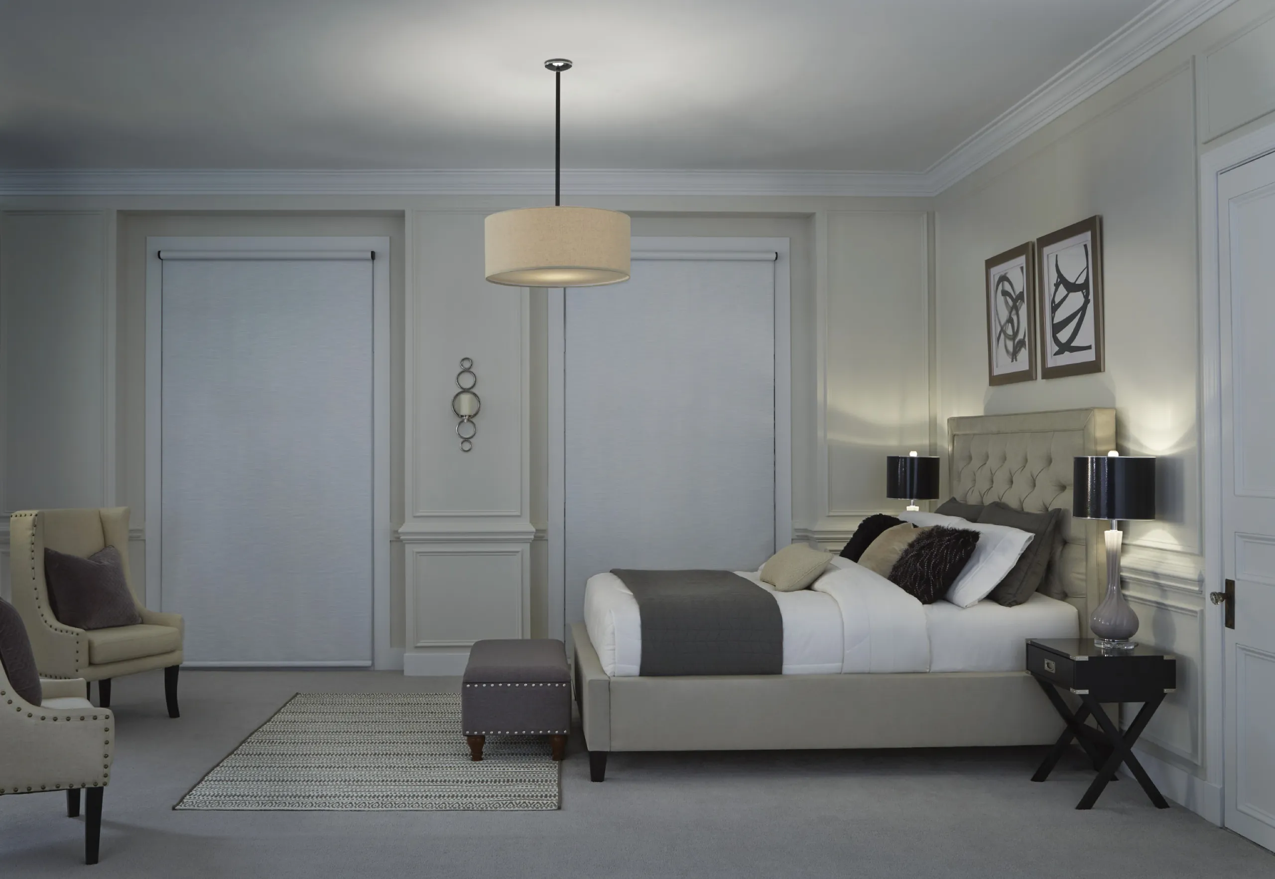 Elegant bedroom at evening with closed silver roller shades, tufted bed, and soft lamp light.