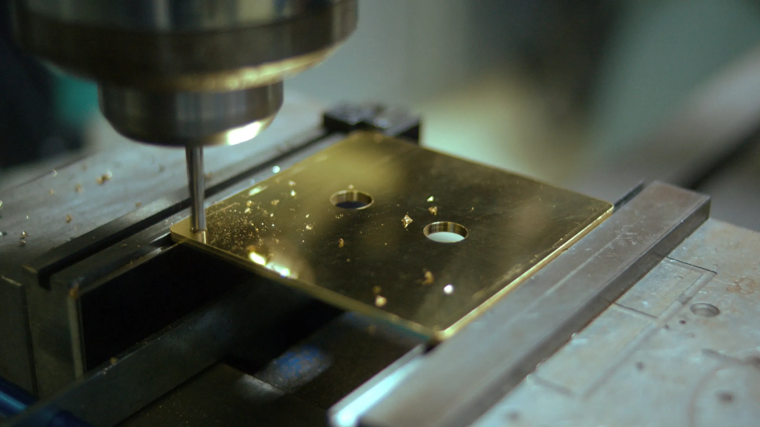 CNC machine milling a polished brass keypad plate with metal chips on the surface.