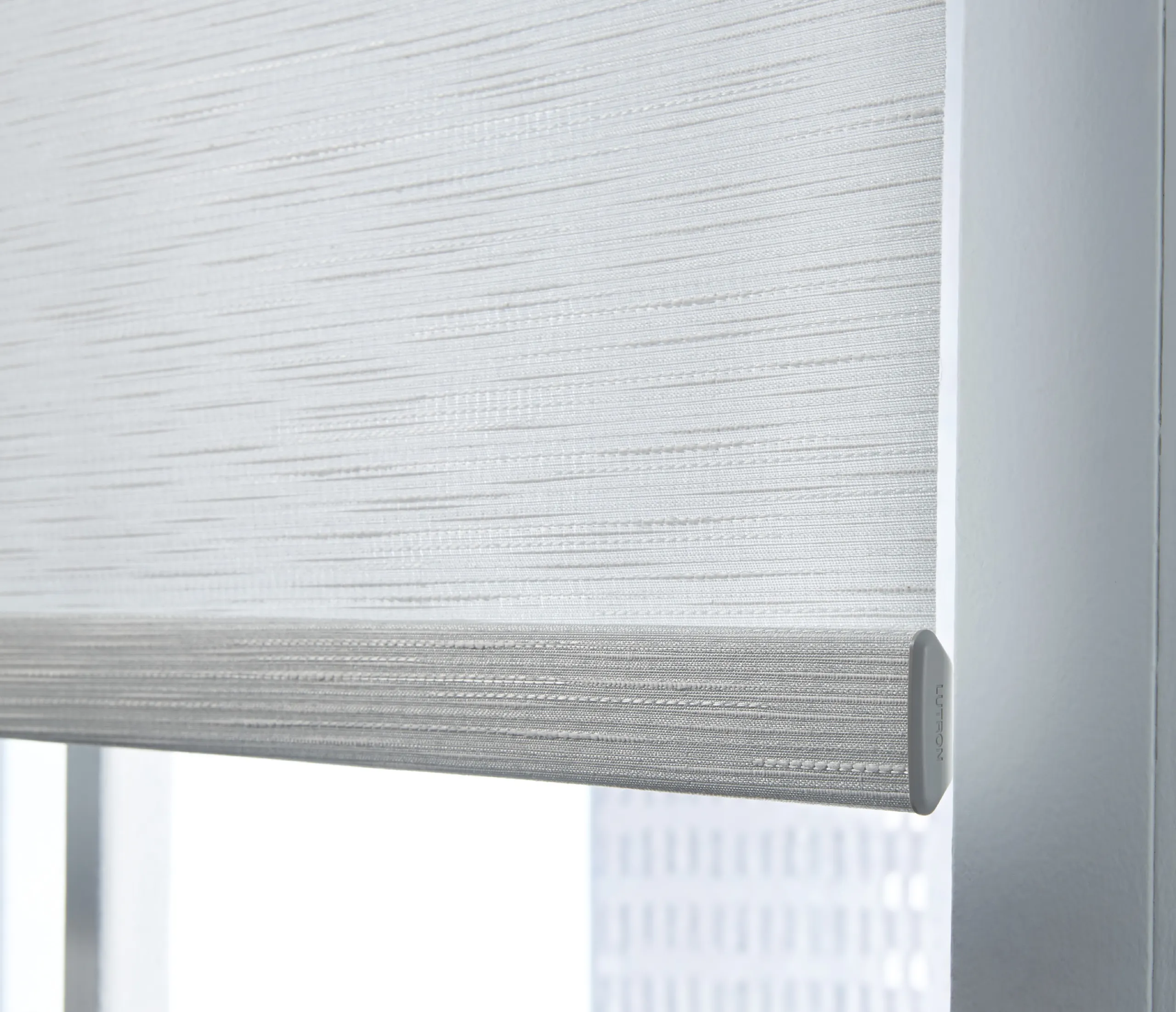 Close-up of a Lutron roller shade hembar and silver textured fabric with an embossed end cap.