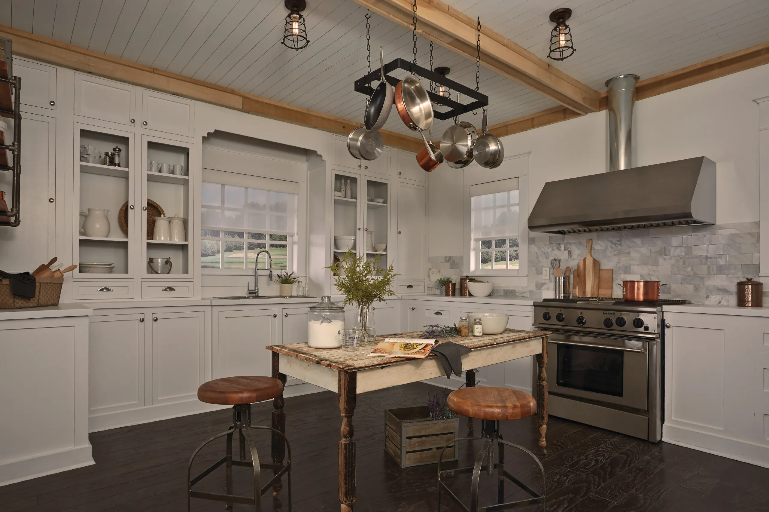 Farmhouse kitchen with white cabinetry, a rustic island, hanging pot rack, and aligned white roller shades.