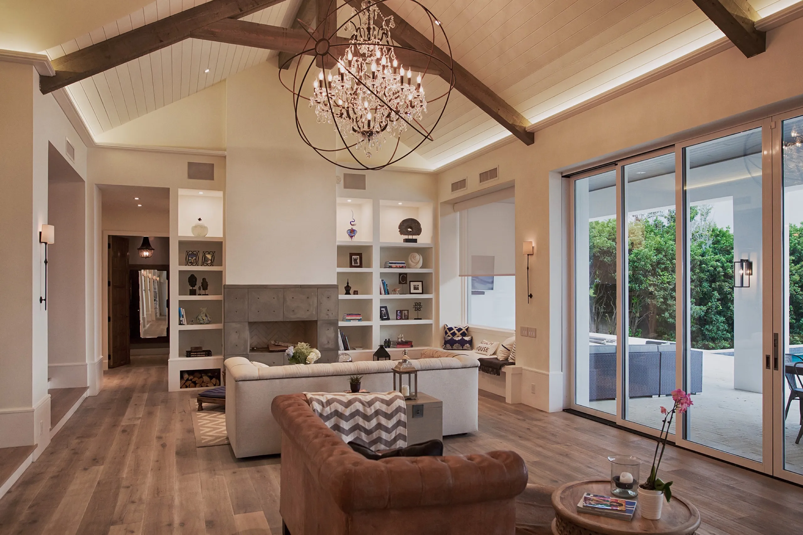 Luxury living room with vaulted wood beams, an orb chandelier, fireplace built-ins, and a partially lowered roller shade.