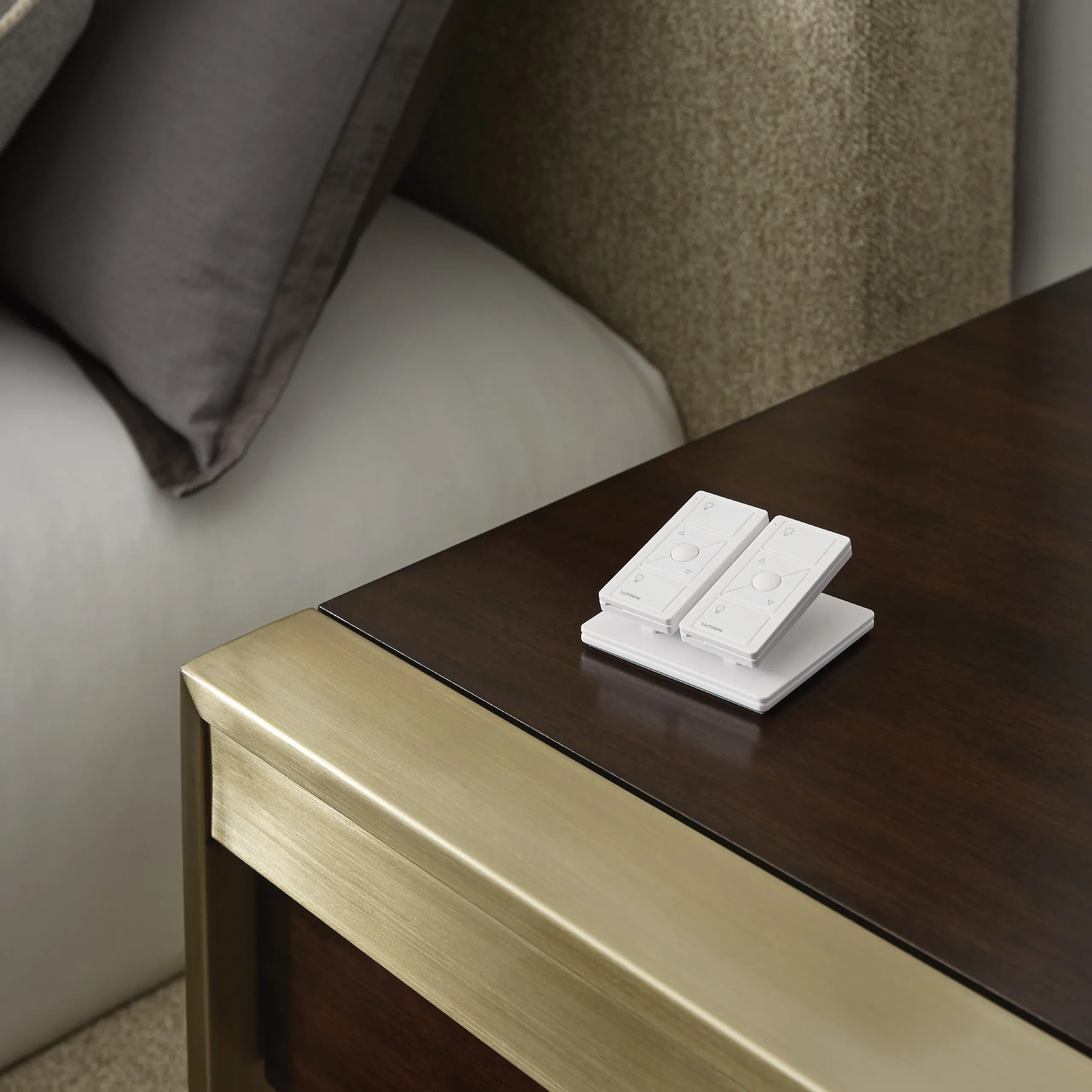 Pair of white Lutron Pico remotes on a pedestal base on a dark wood nightstand with gold trim.