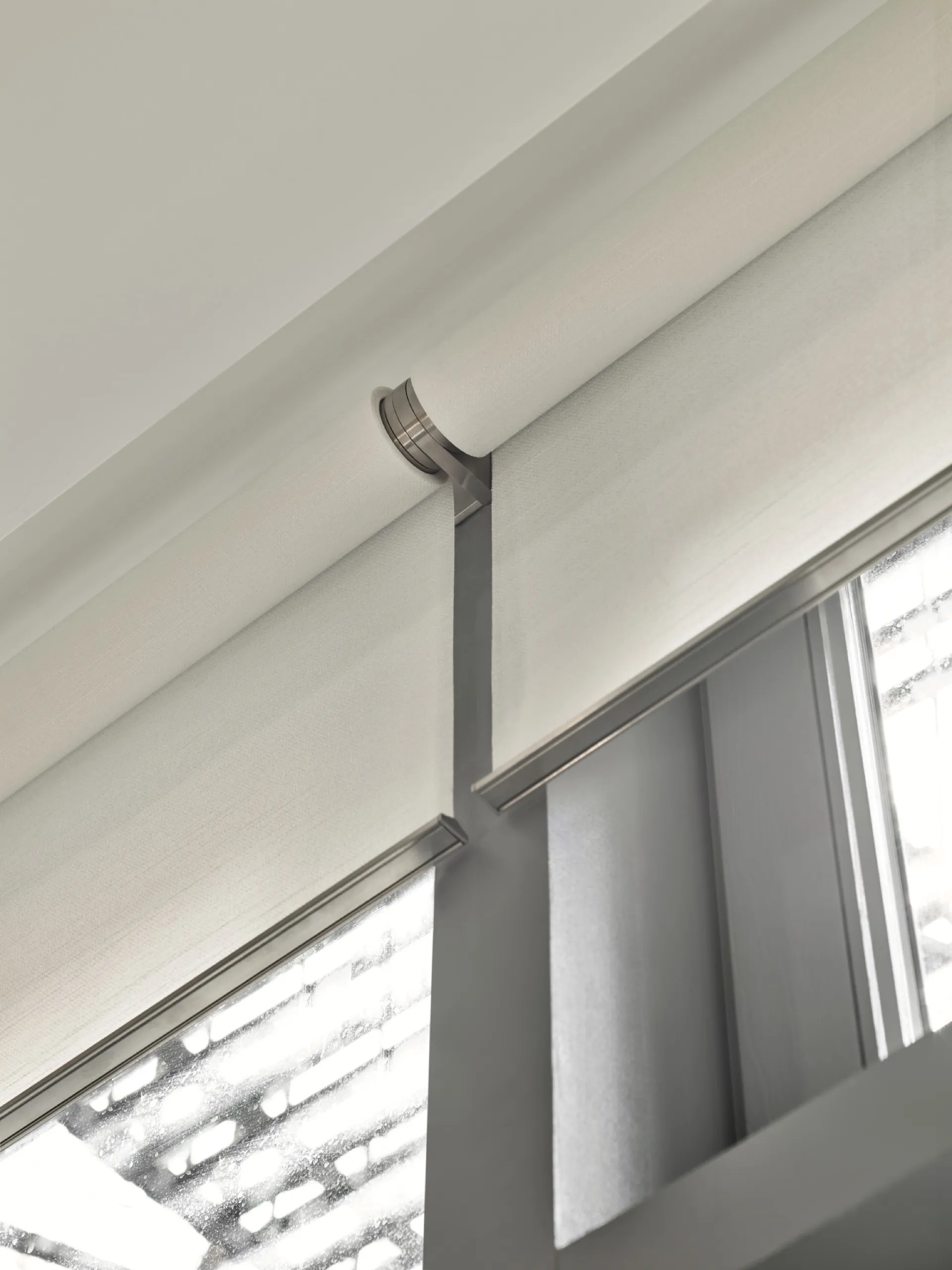 Vertical close-up of a brushed-metal dual roller-shade bracket on a dark loft window frame.
