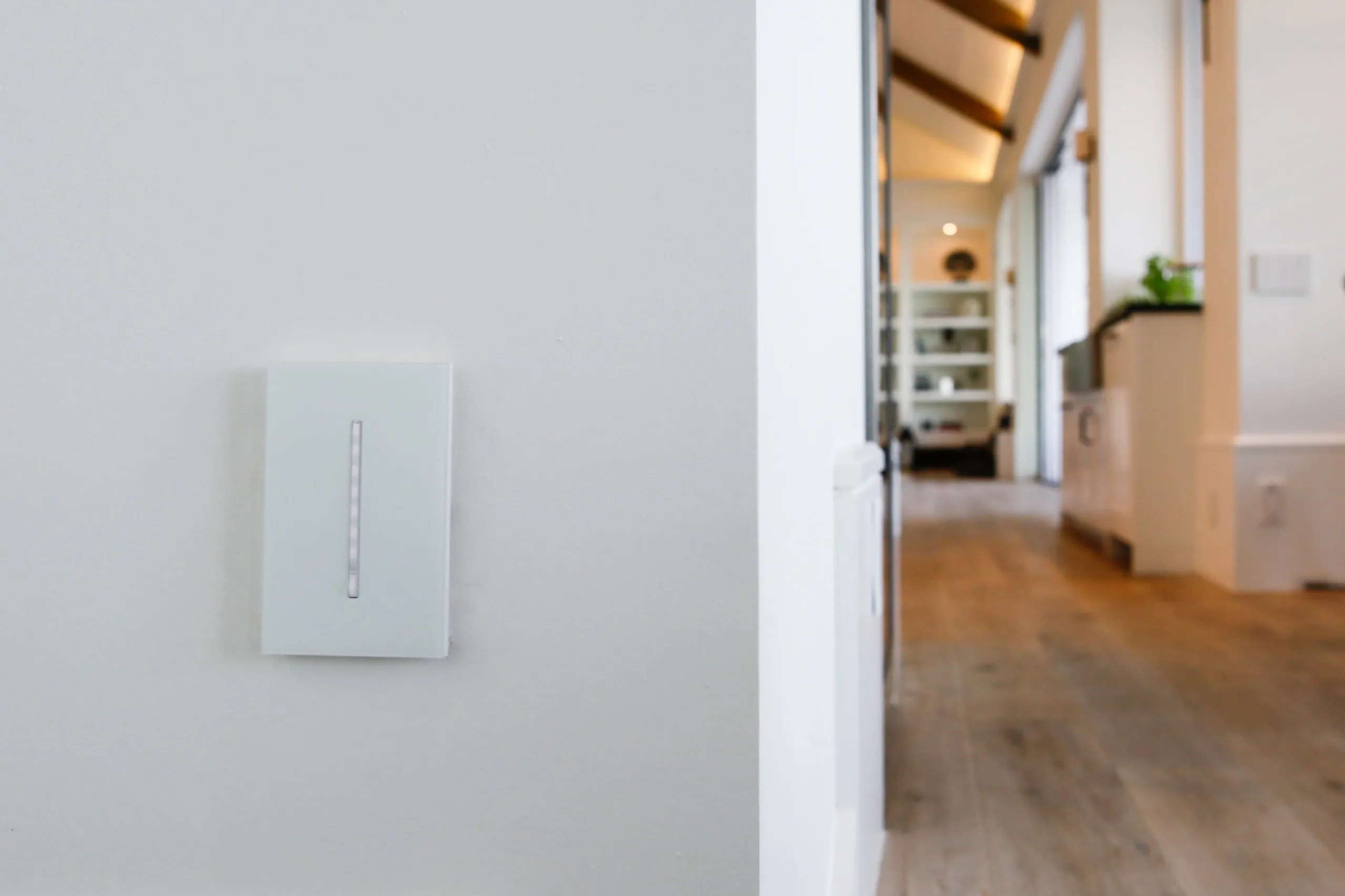 White Lutron Grafik T architectural dimmer on a white wall with a blurred modern kitchen in the background.