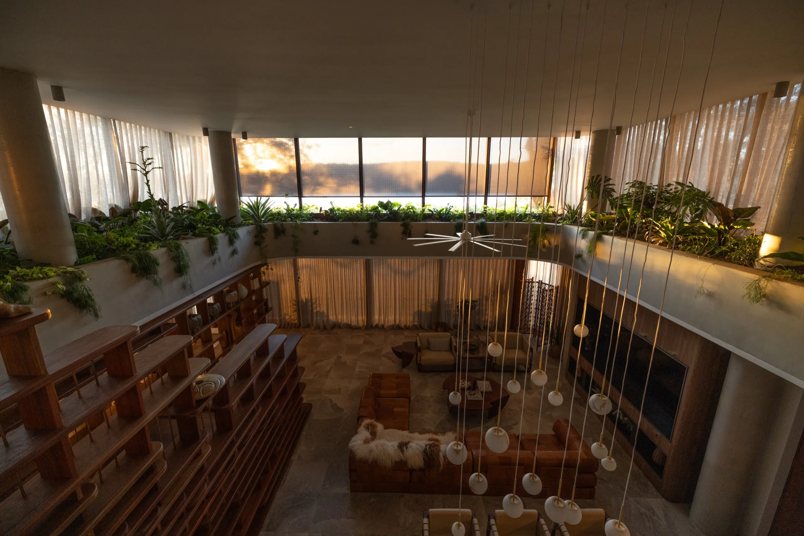 Warm dusk interior of a modern two-story living room with hanging globe lights and dozens of pendants illuminated.