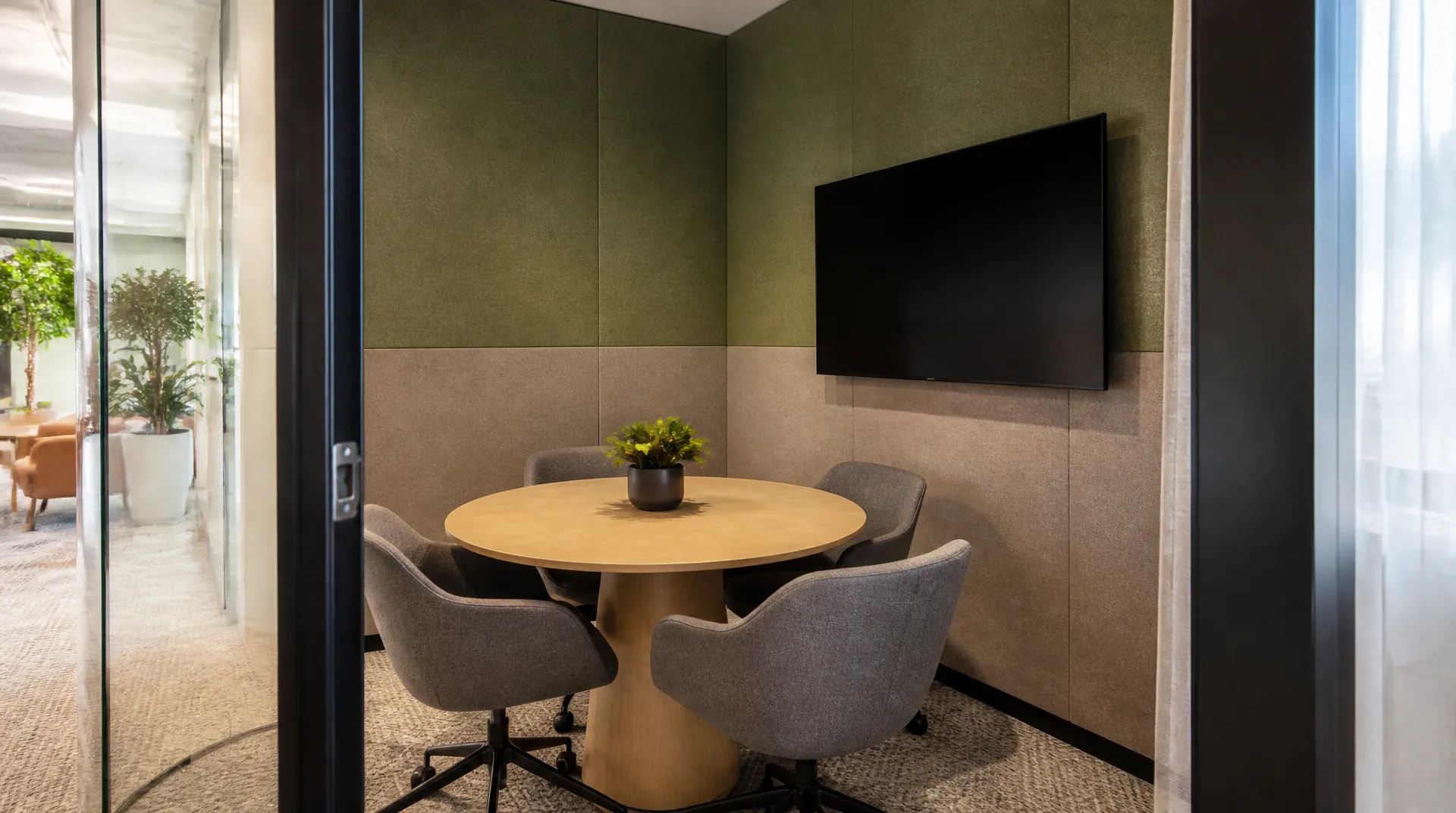 Small huddle room with a round table, four chairs, and an all-in-one video bar beneath a wall display that is switched off.