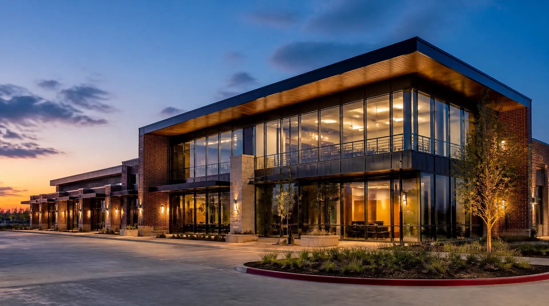 Low-rise commercial office building at dusk with lit windows and landscaped parking.