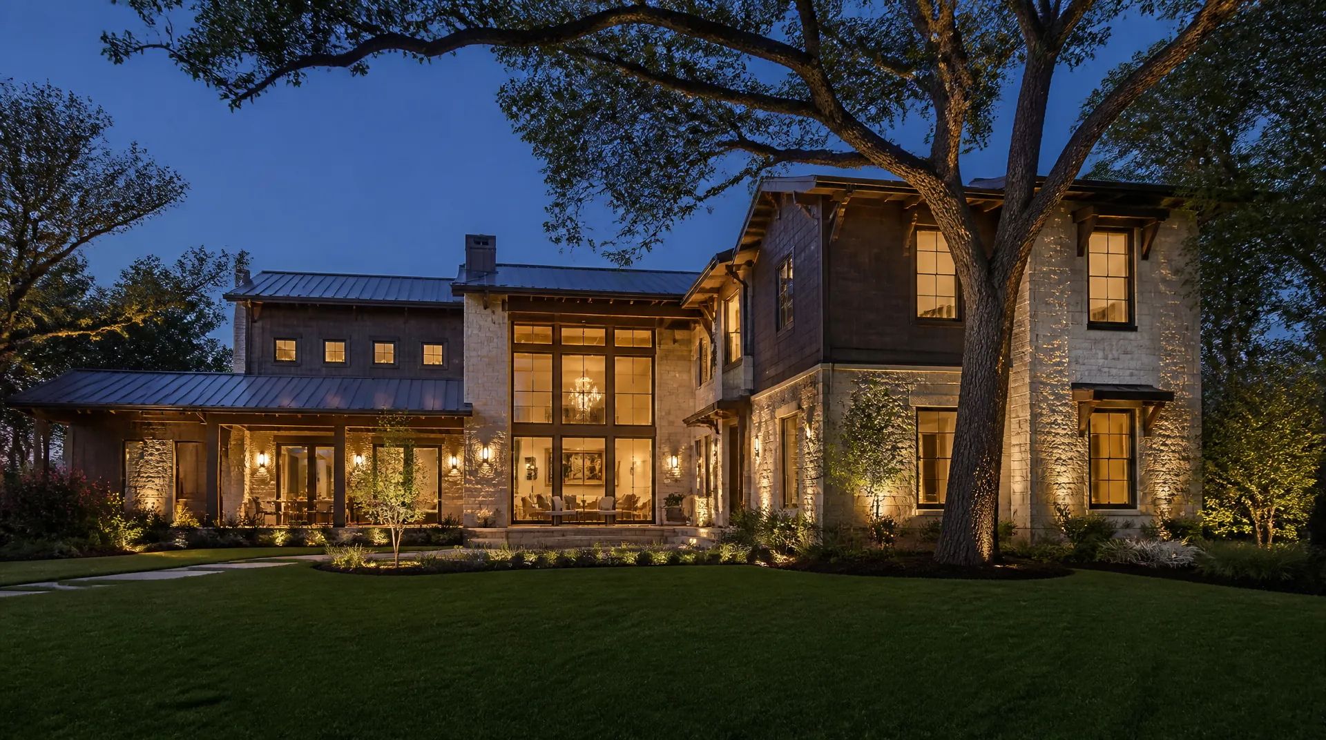 Texas limestone two-story home at blue hour with warm light in the windows and a lit walkway.