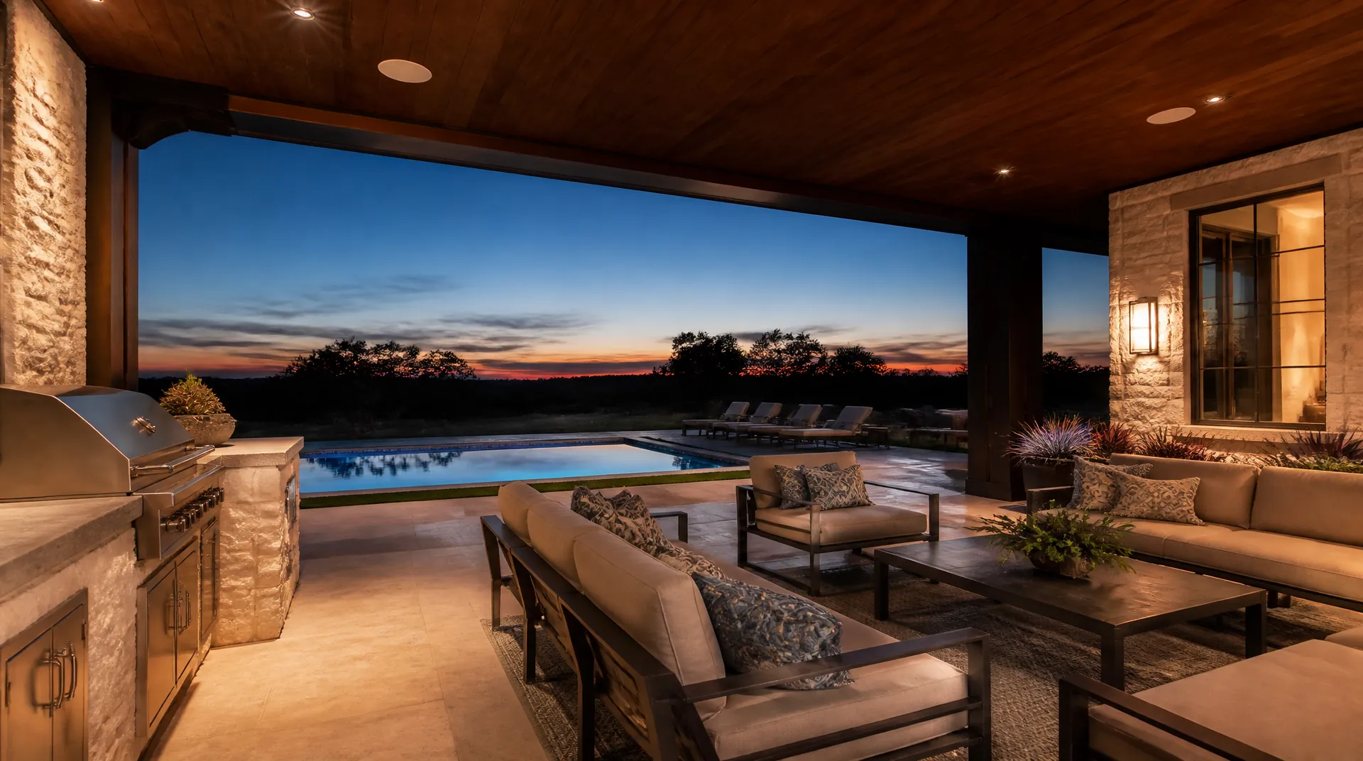 Covered outdoor living area at dusk with flush in-ceiling speakers in a stained wood porch ceiling and a lit pool beyond.