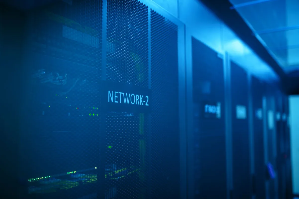 Wall-mounted network cabinet with patch panels and vertical cable managers in a small equipment room.
